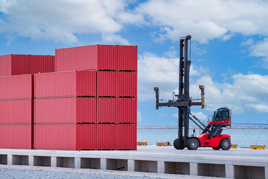 Red straddle carrier in operation at a sea port, efficiently transporting and organizing towering stacks of red shipping containers under a clear blue sky.