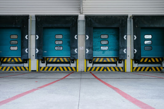 A row of turquoise warehouse loading docks, each with a yellow and black safety pattern, indicating readiness for freight operations.